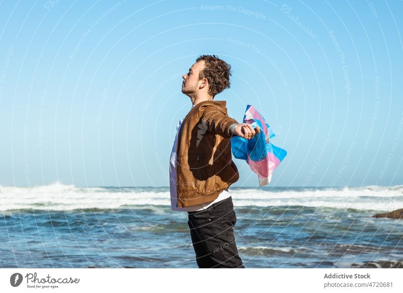 Man with colorful transgender flag near sea man lgbtq identity freedom equal coast nature seashore male beach water wave seaside ocean optimist eyes closed glad