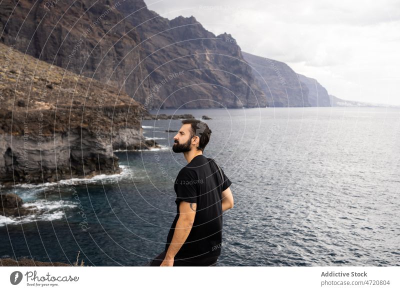 Traveler standing on rocky coast of rippling ocean man tourist freedom admire vacation seascape mountain gloomy wanderlust trip male photo camera traveler shore