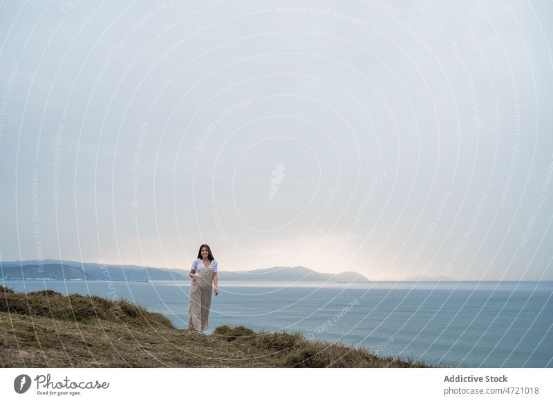 Woman walking on grassy shore woman sea coast nature pastime leisure recreation journey trip female seashore seaside water waterfront waterside summer overall