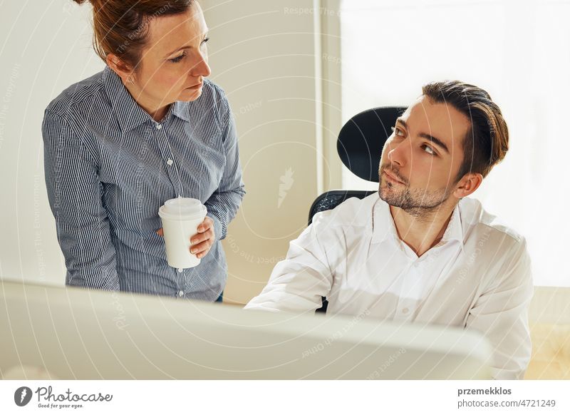 Two business people discussing financial data looking at computer screen. Businesswoman talking to young male coworker in office. People entrepreneurs having conversation working together