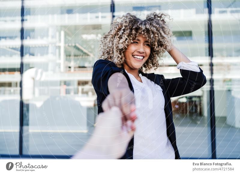 beautiful laughing business woman in city holding hand with friend. Buildings background happy friends afro hispanic mobile phone skyscraper building young