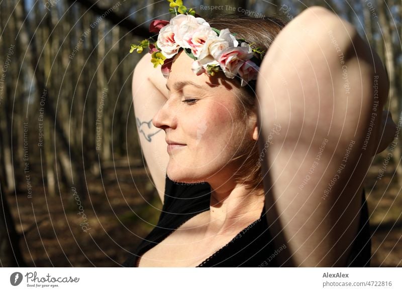 Young woman with flower wreath in hair smiles happily and puts her hands behind her head Woman Smiling Joy pretty daintily fortunate blissfully Happy happiness