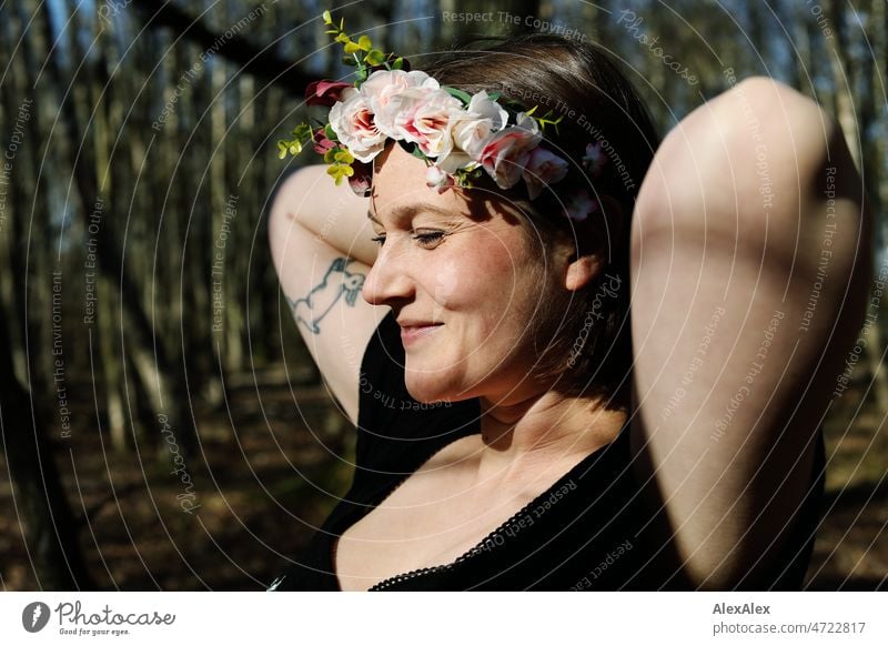 Young woman with flower wreath in hair smiles happily and puts her hands behind her head Woman Smiling Joy pretty daintily fortunate blissfully Happy happiness