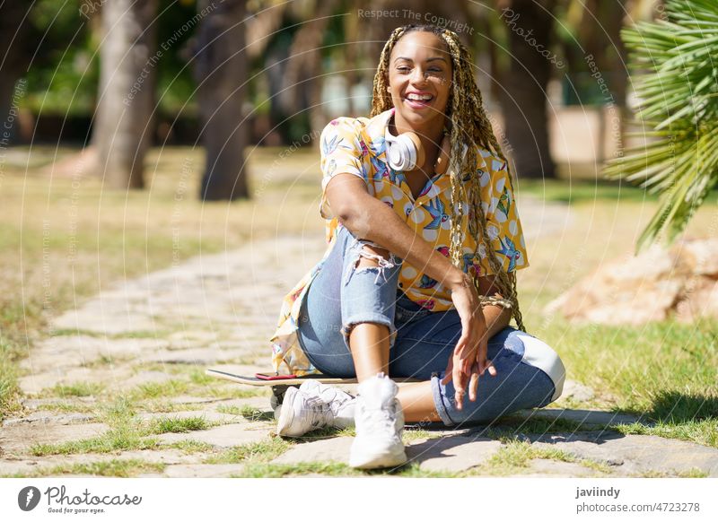 African woman with skateboard relaxing after riding skateboard listening to the music female headphones young girl happy lifestyle street youth urban leisure