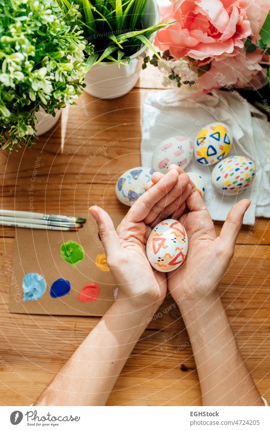 Female holding a modern easter egg. Brushes and paints with flowers and plants. Happy easter concept on a wooden background. hand celebration holiday brush