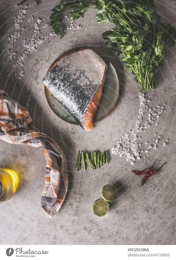 Raw salmon steak with sheds at plate on grey concrete kitchen table raw salt parsley lime olive oil kitchen cloth healthy cooking home fish top view background