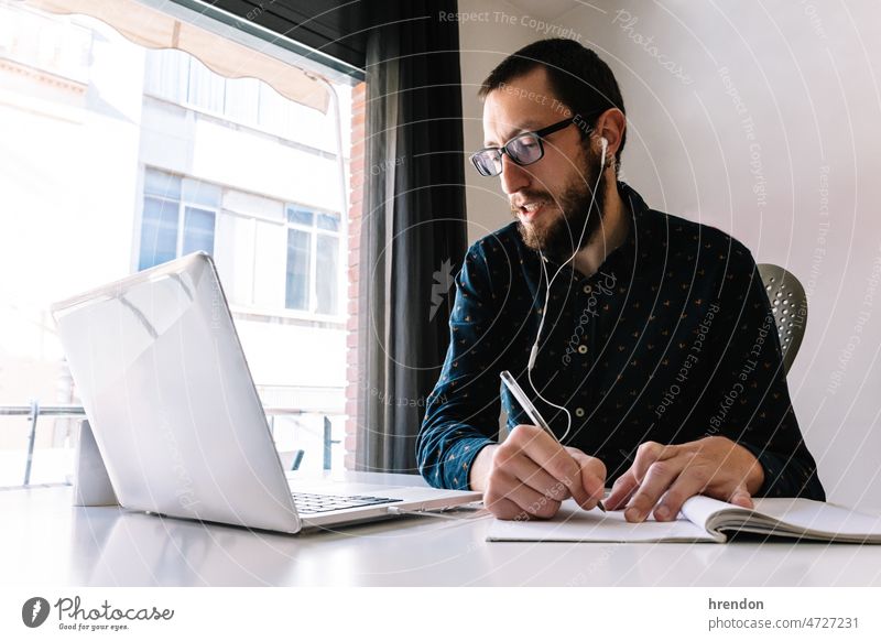 Man working at home and writing down his plan of action home office young adult worker lifestyles small business businessman laptop desk computer technology