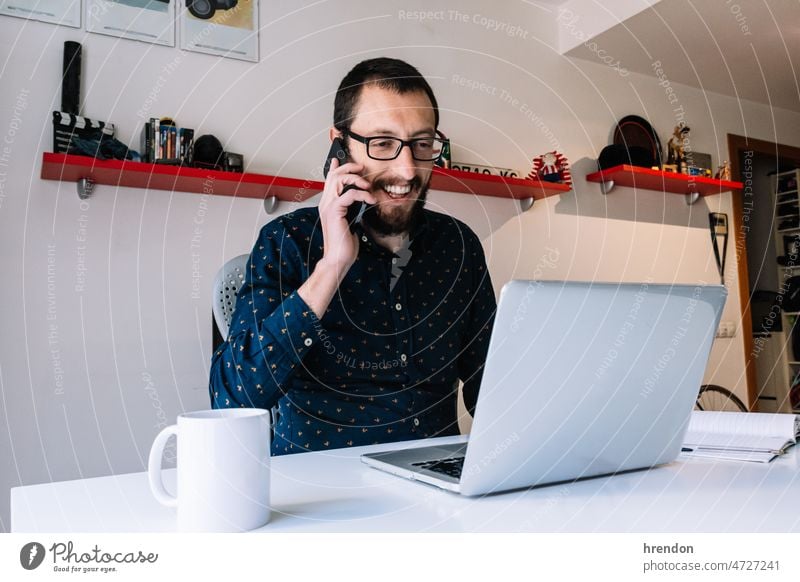 Young man talking on the phone in his home office working young adult worker lifestyles small business businessman laptop desk computer technology