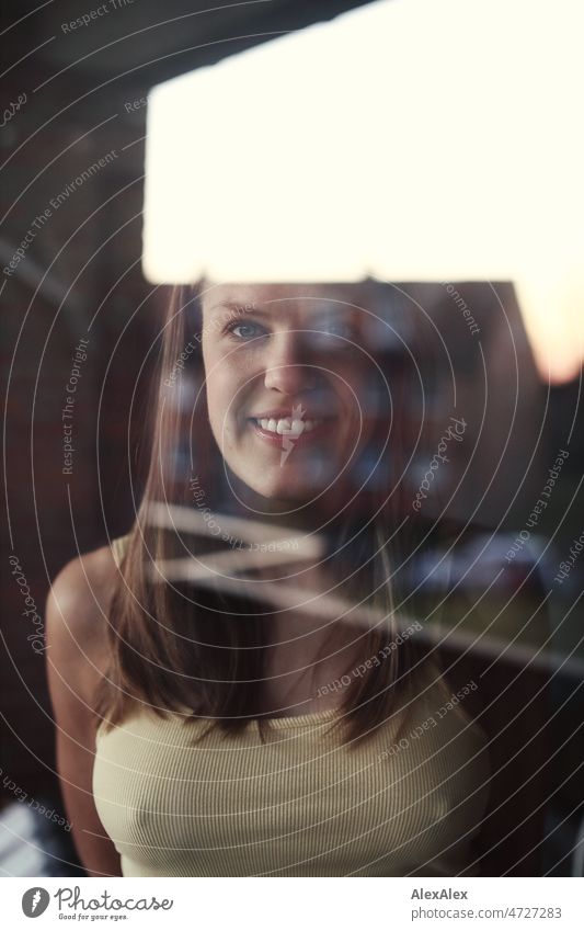 Portrait of a young blonde woman behind a window pane reflecting a house and the evening sky Woman Young woman Blonde portrait Long-haired Smiling Joy Face