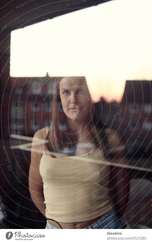 Portrait of a young blonde woman behind a window pane reflecting a house and the evening sky Woman Young woman Blonde portrait Long-haired Smiling Joy Face