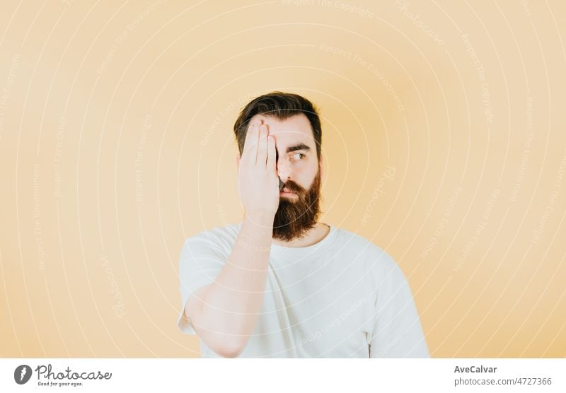 Handsome hipster bearded covering one eye with his hand and looking away from camera. Young man attitude funny. Soft tone color background, expression of normal people. Mockup concept with people