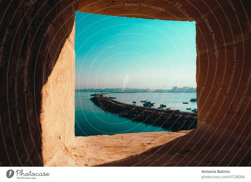 Bay of alexandria city in egypt, as seen from a window at the nearby citadel. Cold morning winter day, stone harbour arch stretching into the distance bridge