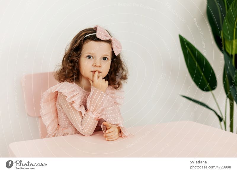 Portrait of a little girl in festive clothes sitting thoughtfully at a table looking thinking child desk kid curious young female portrait idea lovely person