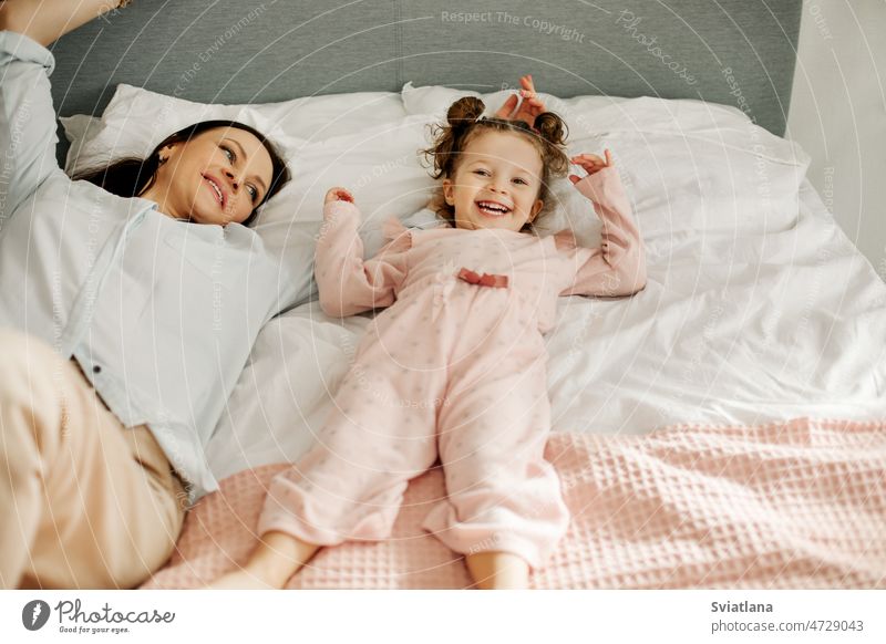 Mom and daughter are lying on the bed and smiling. Mom and baby are having fun on the bed. Happy loving family mom playing young girl child bedroom happy mother