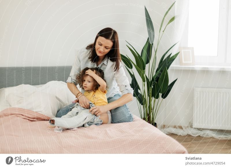 A young mother helps her little daughter to change clothes. Taking care of children, help, motherhood mom dressing up baby girl home together parenting happy