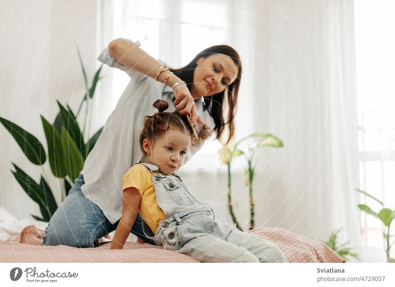 A happy mom combs her little daughter's hair while sitting in bed in the morning mother baby family hairbrush girl childhood lifestyle young cheerful happiness