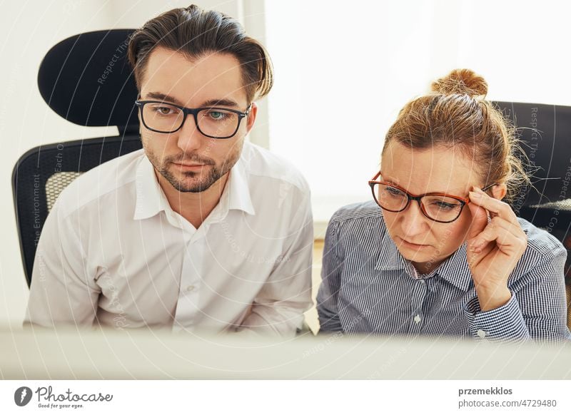 Two business people discussing financial data looking at computer screen. Entrepreneurs working hard sitting at computere screen in office. People having deadline working together