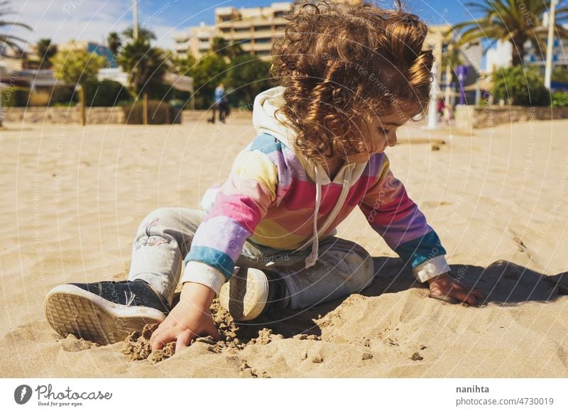 Young toddler playing with the sand at the beach alone enjoy summer explore parenting freedom happy rainbow happiness scene curly hair kid child baby childhood