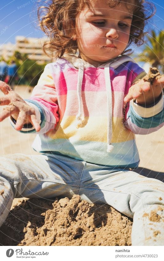 Young toddler playing with the sand at the beach alone enjoy summer explore parenting freedom happy rainbow happiness scene curly hair kid child baby childhood