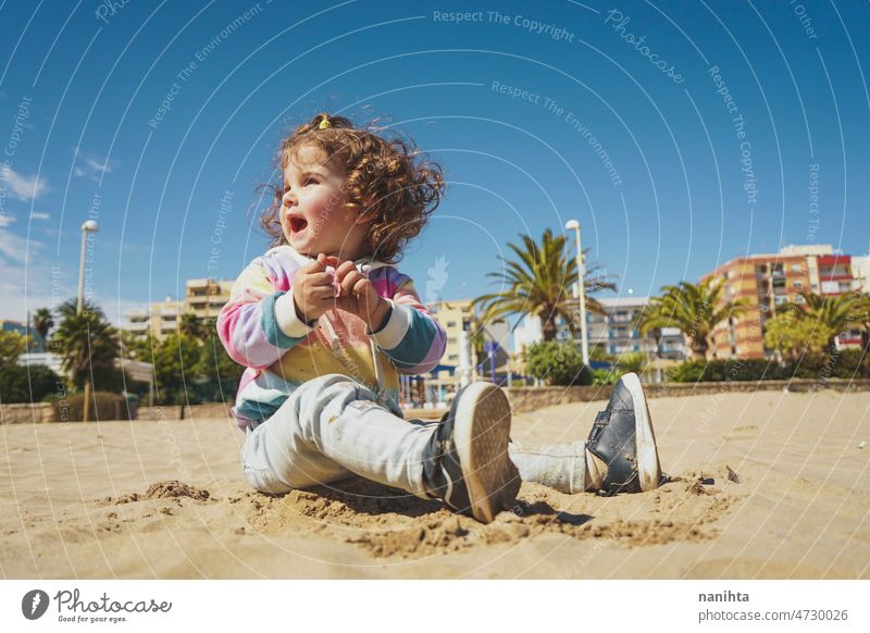 Young toddler playing with the sand at the beach alone enjoy summer explore parenting freedom happy rainbow happiness scene curly hair kid child baby childhood