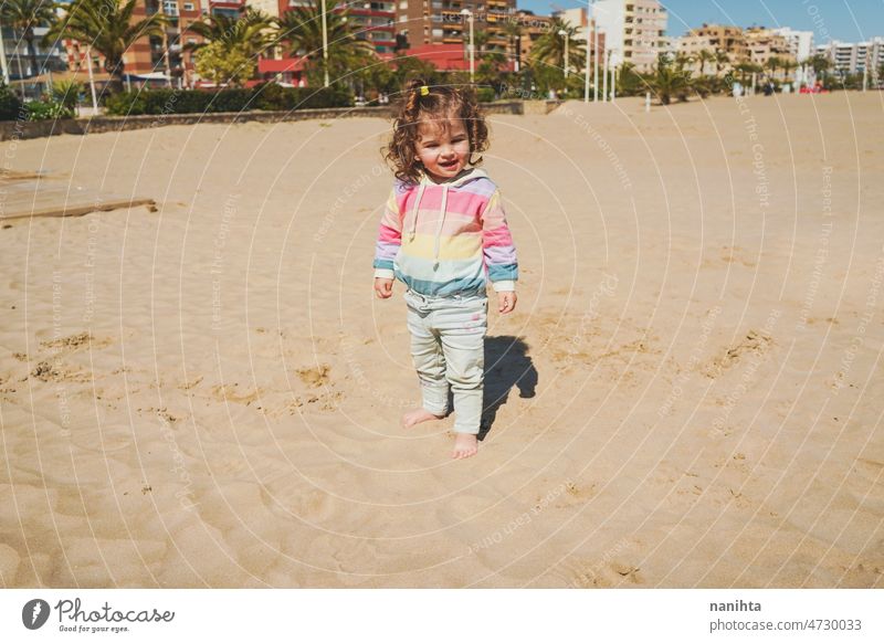 Young toddler playing with the sand at the beach alone enjoy summer explore parenting freedom happy rainbow happiness scene curly hair kid child baby childhood