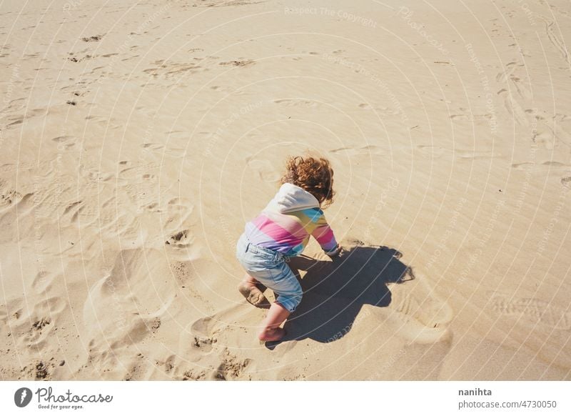 Young toddler playing with the sand at the beach alone enjoy summer explore parenting freedom happy rainbow happiness scene curly hair kid child baby childhood