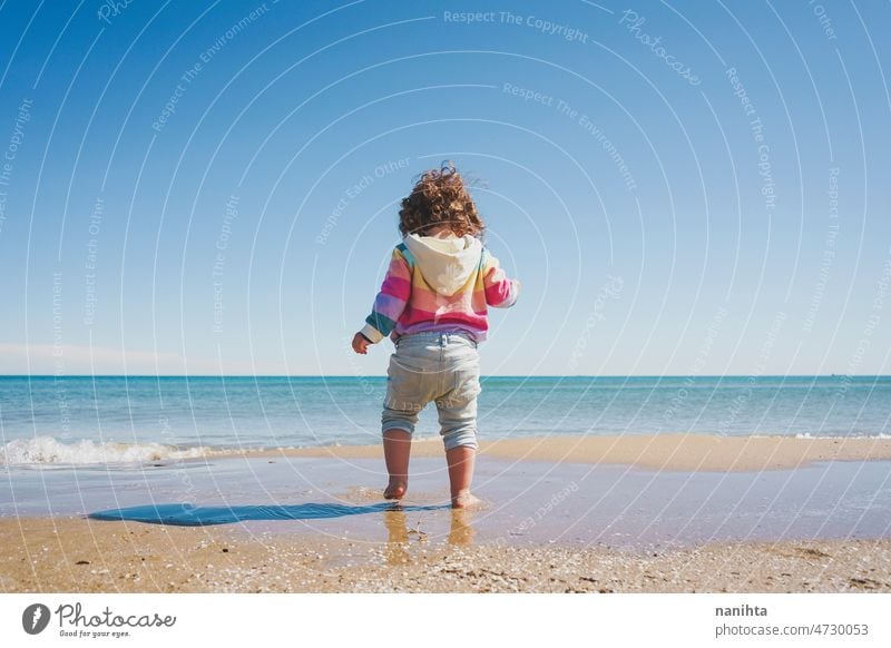 Wide view of a little girl wearing rainbow hoodie playing at the beach freedom happiness holidays baby toddler family sea shore playful real lifestyle people