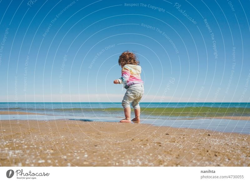 Wide view of a little girl wearing rainbow hoodie playing at the beach freedom happiness holidays baby toddler family sea shore playful real lifestyle people