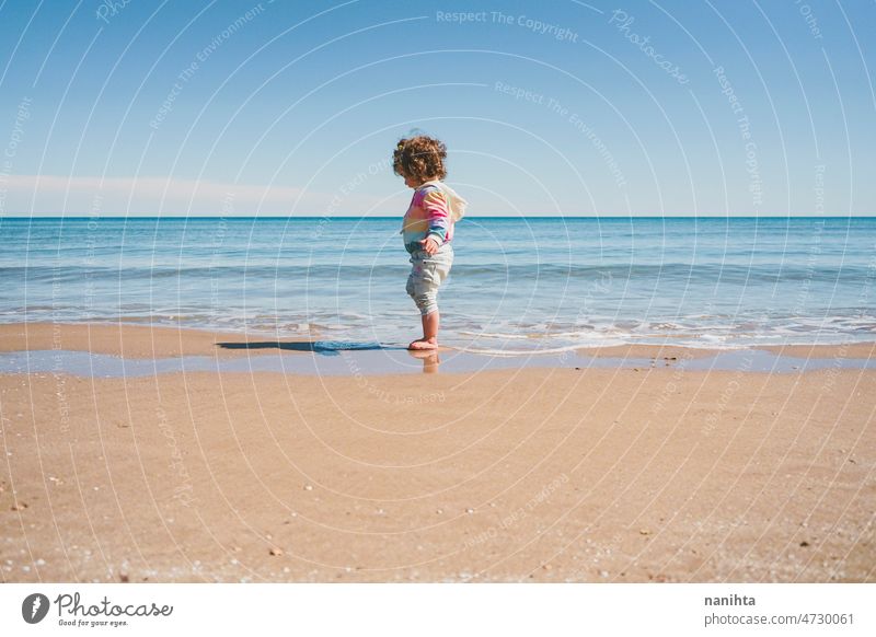 Wide view of a little girl wearing rainbow hoodie playing at the beach freedom happiness holidays baby toddler family sea shore playful real lifestyle people