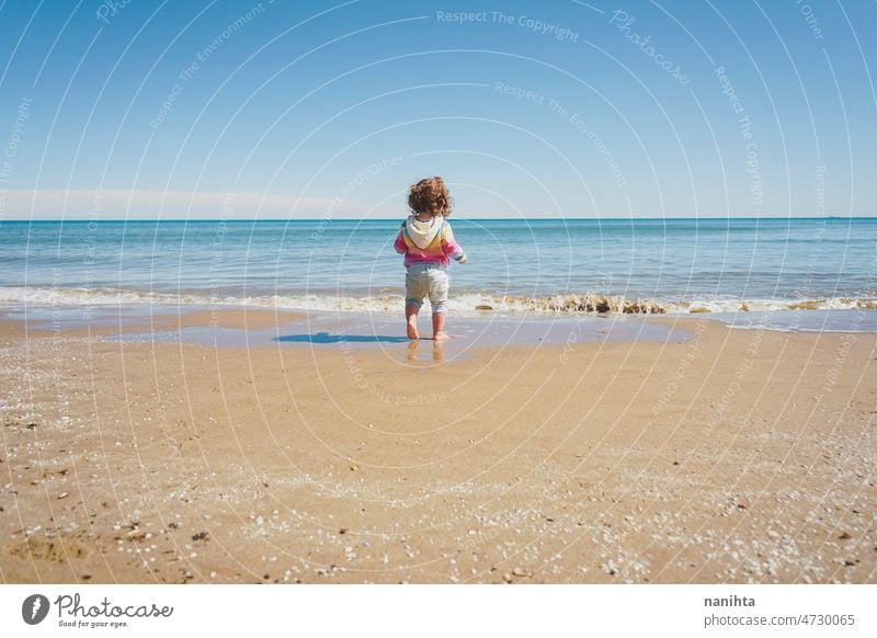 Wide view of a little girl wearing rainbow hoodie playing at the beach freedom happiness holidays baby toddler family sea shore playful real lifestyle people