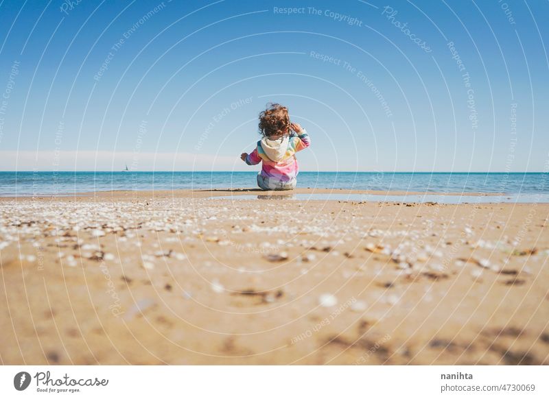 Wide view of a little girl wearing rainbow hoodie playing at the beach freedom happiness holidays baby toddler family sea shore playful real lifestyle people