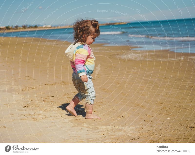 Wide view of a little girl wearing rainbow hoodie playing at the beach freedom happiness holidays baby toddler family sea shore playful real lifestyle people