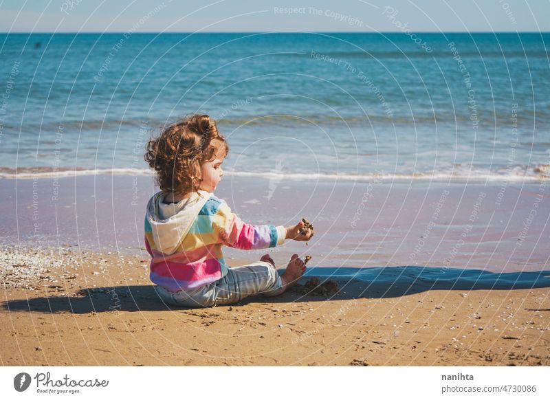 Wide view of a little girl wearing rainbow hoodie playing at the beach freedom happiness holidays baby toddler family sea shore playful real lifestyle people