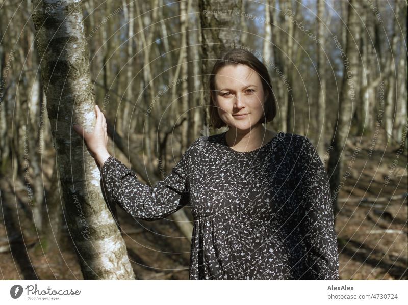 Analog portrait of a young pregnant woman standing in a deciduous forest leaning on a tree Smiling vigorous Grass Woodground trees youthful Model Esthetic