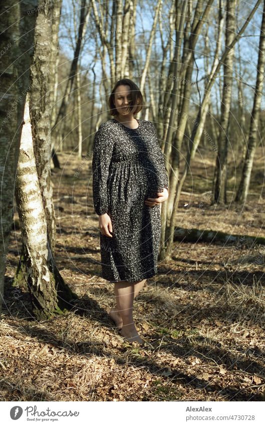 Analog full body portrait of young pregnant woman standing barefoot in a deciduous forest holding her baby belly with one hand Smiling vigorous Grass Woodground