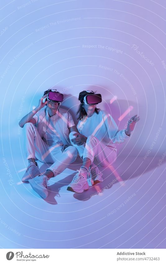 Couple in VR headset sitting near wall couple vr virtual reality cyberspace future augmented reality interactive technology explore goggles futuristic studio