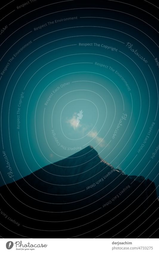 Three small white clouds over the dark mountain top. A little sun can be glimpsed on one side, with otherwise in the delicate sky blue. Mountain Sky Clouds