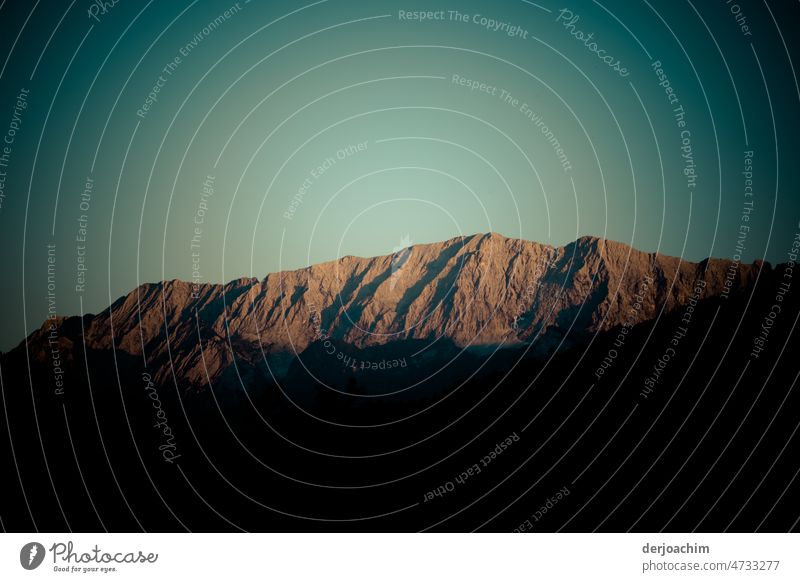 The mountains in the last evening light. A cloudless sky underlines the whole. Part of the mountain is already in darkness. Sunset Sky Stripe Light Nature