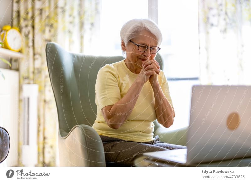 Senior woman using laptop at home glasses eyeglasses spectacles alone domestic life elderly female grandma grandmother grey hair house indoors lifestyle mature