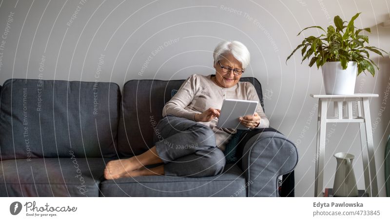 Senior woman using a digital tablet at home online internet modern technology communication connection living room glasses eyeglasses spectacles alone