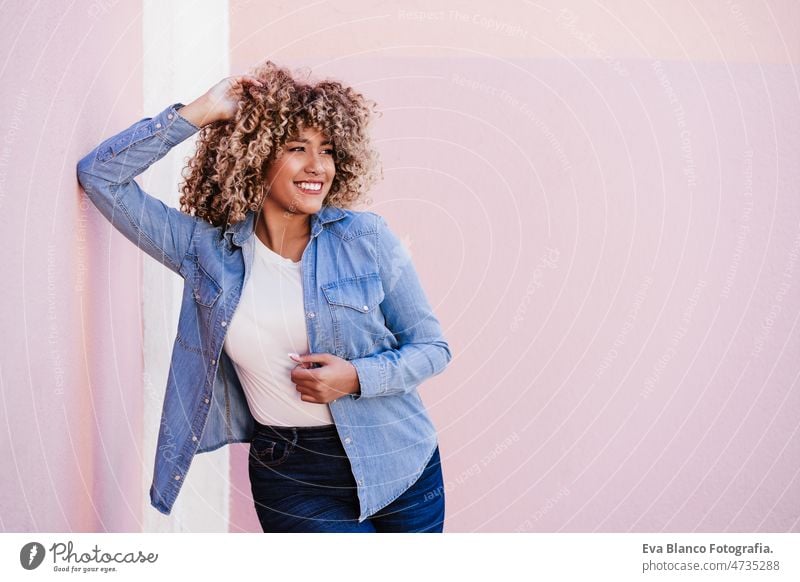 portrait of confident curvy hispanic woman outdoors in spring. pink wall. Body positivity body positivity size happy afro smiling city eyes closed