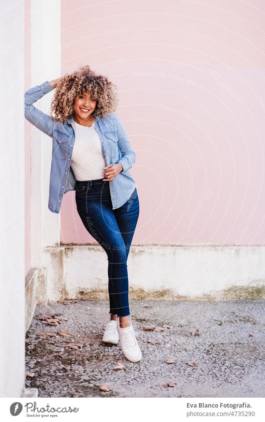 portrait of confident curvy hispanic woman outdoors in spring. pink wall. Body positivity body positivity size happy afro smiling city eyes closed