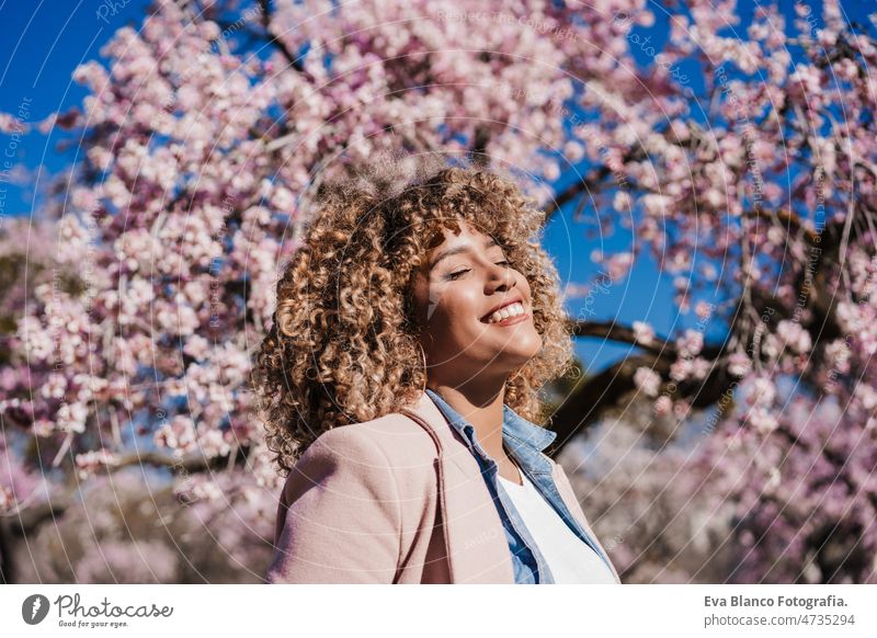 smiling hispanic woman with eyes closed in park enjoying sunny day. Spring flowers background dancing curvy body positivity afro happy spring size portrait