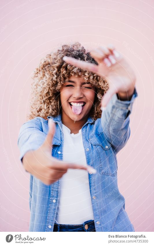 portrait of confident curvy hispanic woman outdoors in spring. pink wall. Body positivity frame body positivity size happy afro smiling city eyes closed