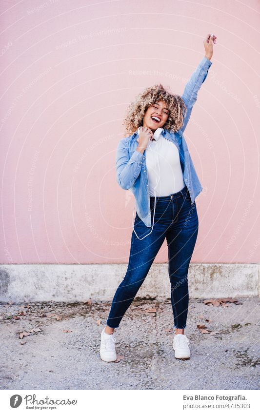 happy curvy hispanic woman with afro hair in city using mobile phone and headset. Body positivity listening body positivity selfie technology internet wireless