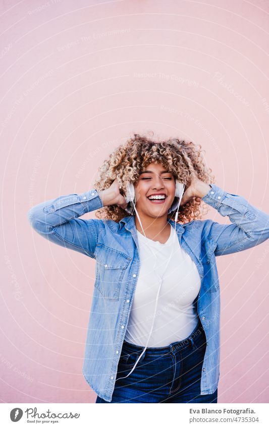 happy curvy hispanic woman with afro hair in city using mobile phone and headset. Body positivity listening body positivity selfie technology internet wireless