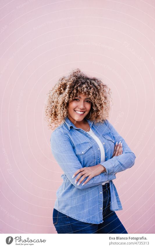 portrait of confident curvy hispanic woman outdoors in spring. pink wall. Body positivity arms crossed body positivity size happy afro smiling city eyes closed