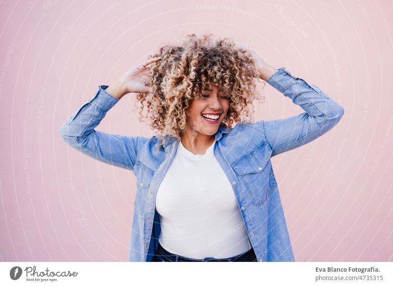 portrait of beautiful curvy hispanic woman, afro hair outdoors in spring. pink wall. Body positivity body positivity size happy smiling city eyes closed