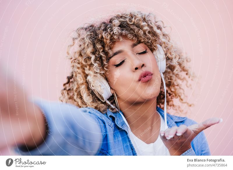 happy curvy hispanic woman with afro hair in city using mobile phone and headset. Body positivity listening body positivity technology internet wireless picture