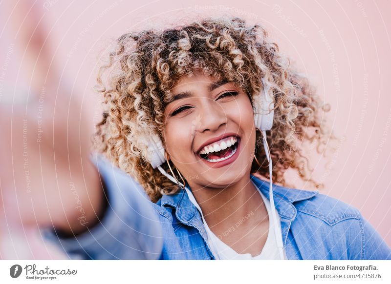 happy curvy hispanic woman with afro hair in city using mobile phone and headset. Body positivity listening body positivity technology internet wireless picture